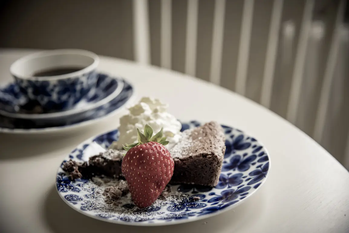 kaffekopp och en assiett med kladdkaka med grädde och jordgubbe