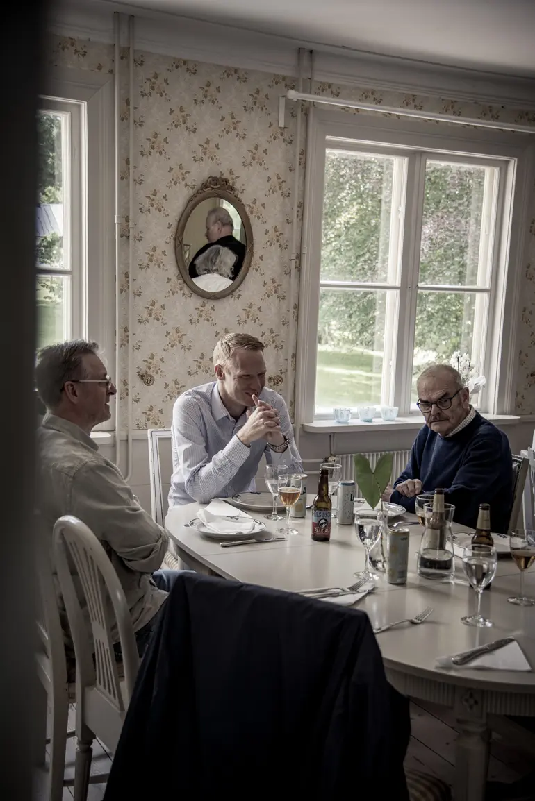 tre män äter lunch runt ett ovalt bord på herrgården